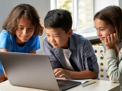 3 children sitting while looking at a laptop